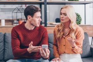 emotional young couple quarreling about smartphone at home, jealousy concept