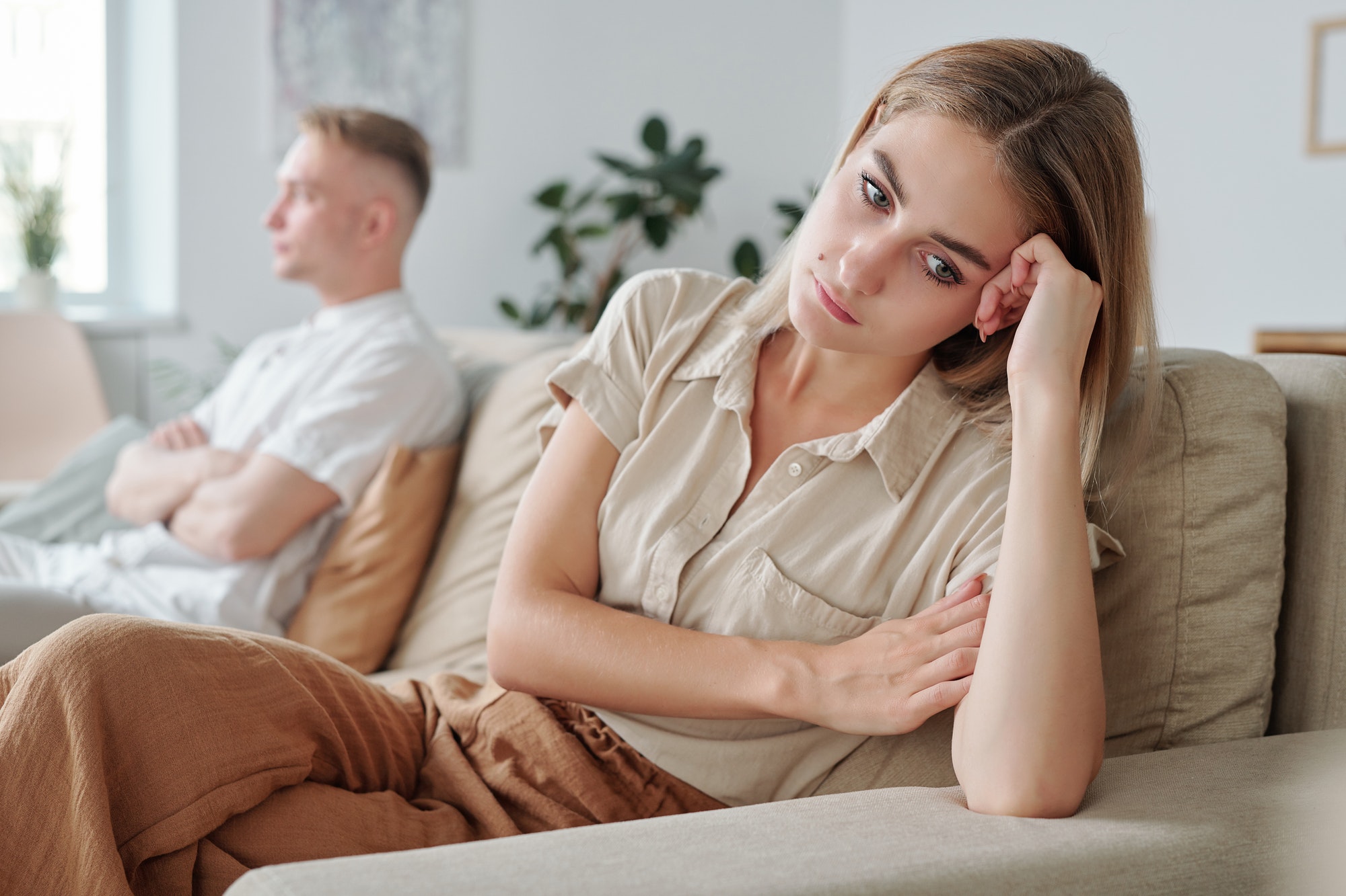 Young upset and lonely wife sitting on couch while expressing offense to husband