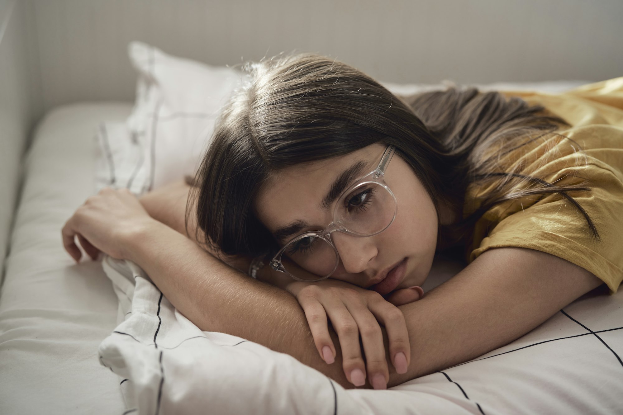 Sad caucasian teenage girl lying on bed and looking away with anxiety