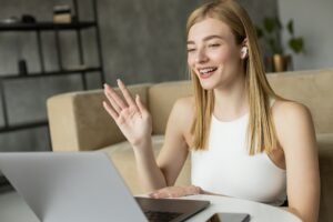 Smiling blonde coach in earphone having video call on laptop at home
