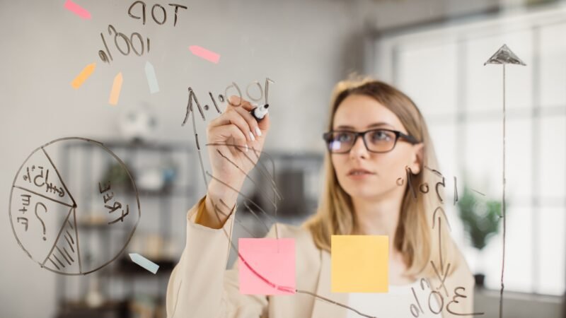 Focused business woman writing on glass board at office